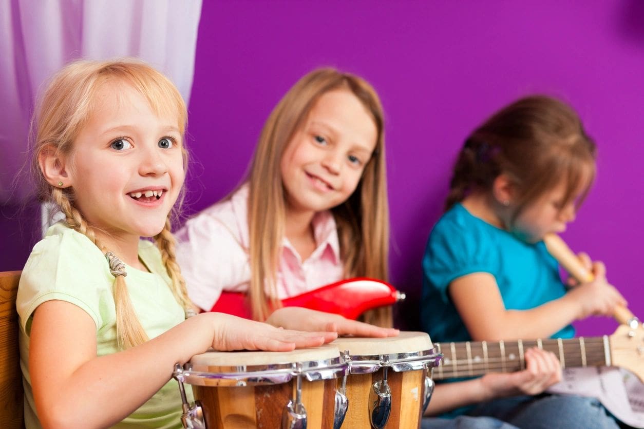 Three children are playing musical instruments in a room.